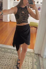 Minifalda negra con diseño pareo, de corte asimétrico y nudo lateral.