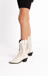 Botas tejanas de cuero color blanco hueso con bordados decorativos en hilo plateado, taco bajo y cierre lateral. Forradas en neoprene para mayor comodidad.