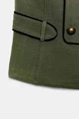 Chaleco verde militar con cuello halter, espalda descubierta y cierre frontal con cremallera oculta. Presenta detalles de falsos botones dorados y ribetes en contraste, con trabillas en los laterales.