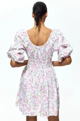 Vestido corto de algodón con estampado floreado en tonos rosados y lilas sobre base blanca. Presenta escote en V fruncido, mangas globo a los codos con puños elásticos y sección fruncida en la cintura.