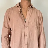 Camisa de lino con corte oversize, cuello clásico y cierre frontal con botones. Presenta mangas largas con puños arremangados y una textura rústica característica del tejido.