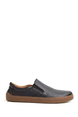 Zapatilla slip-on de cuero negro con textura granulada, diseño barefoot y suela plana de goma color marrón.