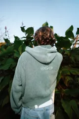Campera con capucha de tejido de punto acanalado en color verde, con cierre frontal completo, bolsillos tipo canguro y detalles de efecto desgastado en los bordes.