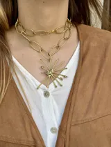 Collar de doble cadena en bronce con dije central de diseño abstracto en forma de estrella o rayos.