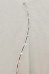 Chaqueta de punto color beige claro, de cuello redondo y manga larga abullonada con puño ajustado. Cierre frontal cruzado con botones plateados.