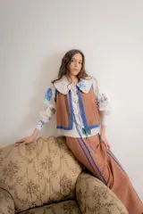 Chaleco tejido sin mangas, color negro, con textura brillante (lurex) y ribetes en azul. Presenta un escote redondo y se ata al frente con cordones.