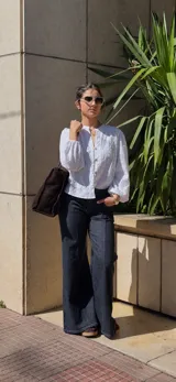 Camisa blanca de broderie con cuello redondo, cierre frontal con botones de madera y mangas largas abullonadas con puños elásticos.