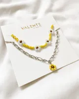 Set de dos collares: uno de cuentas amarillas y blancas con forma de flores, y otro de cadena plateada con dije de flor amarilla.