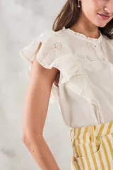 Blusa sin mangas color crema con bordado floral, cuello mao y volados en los hombros.