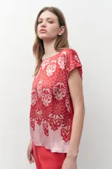 Blusa de satén con estampado floral bicolor en tonos rojo y rosado, de corte recto, cuello redondo y mangas cortas.