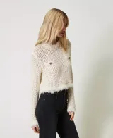 Sweater de punto calado color crema, con cuello redondo, manga larga, flecos en el ruedo y dos bolsillos de parche con botones metálicos con el logo de la marca.