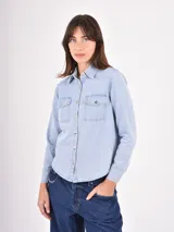 Camisa de jean en tono celeste claro, con cuello clásico, cierre frontal con botones metálicos y dos bolsillos frontales con solapa.