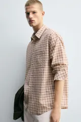 Camisa de corte relajado confeccionada en tejido fluido con algodón. Presenta un diseño de cuadros, cuello solapa, manga larga con puño abotonado, bolsillo plastrón en el pecho y cierre frontal con botones.