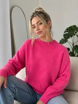 Sweater de punto color fucsia, con cuello redondo, mangas largas y diseño holgado. Presenta detalles de tejido desgastado o con pequeñas roturas decorativas en el frente.