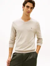 Sweater Tommy Hilfiger de cuello en V y manga larga, color beige, confeccionado en mezcla de algodón y poliéster. Presenta puños y bajo de punto canalé, con el logo de la marca bordado en el pecho.
