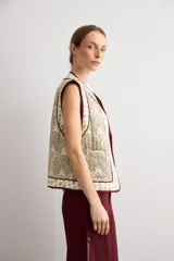 Chaleco capitoneado sin mangas, color crudo con estampado paisley y bordes ribeteados en tono bordó.
