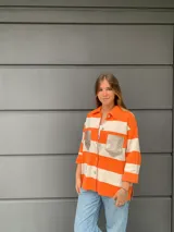 Camisa tejida a rayas horizontales color naranja y blanco, con cuello camisero, mangas tres cuartos y bolsillos frontales con solapa en color dorado.