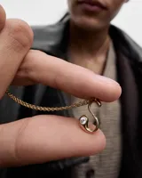 Collar de oro con dije de letra S que incluye una circonia incrustada en el extremo inferior, suspendido de una fina cadena de eslabones.