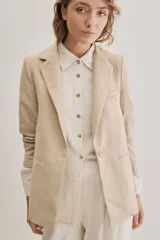 Blazer sastrero de lino color beige, de silueta relajada y líneas clásicas. Incorpora solapas tradicionales, cierre frontal de un botón y bolsillos de vivo.