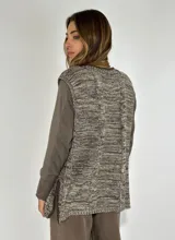 Chaleco de punto con diseño de trenzas, cuello redondo y aberturas laterales en el ruedo. Presenta un patrón jaspeado en tonos marrones y beige.