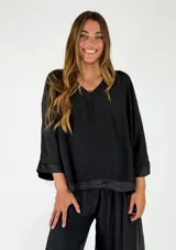 Blusa Verona de viscosa, color negro, con escote en V y mangas tres cuartos con detalles de satén en los puños y en el ruedo.