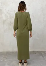 Vestido largo color verde militar, con cuello redondo, mangas largas abullonadas con puños elásticos y detalle de lazo anudado en la cintura. Presenta una abertura lateral en la falda.