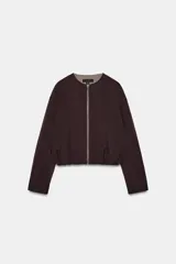 Chaqueta estilo bomber de color marrón oscuro, con cuello redondo, manga larga y cierre frontal con cremallera. Presenta bolsillos delanteros de vivo y un diseño con bajo fruncido.