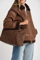 Campera tipo gamulán de corte oversize, color marrón con interior y cuello de corderito sintético oscuro. Presenta cierre frontal, detalles de costuras reforzadas y terminaciones en puños y ruedo con corderito a la vista.