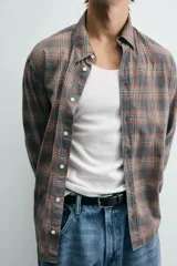 Camisa de corte relajado confeccionada en algodón, con estampado de cuadros en tonos marrones y grises. Presenta cuello abotonado, cierre frontal de botones y mangas largas con puños abotonados.