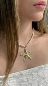 Gargantilla tipo choker con cordón trenzado color crema y dije central de estrella de mar en tono dorado con textura detallada.