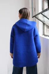 Tapado de paño color azul con capucha, cierre frontal y detalles en color beige en el interior de la capucha, puños y bordes de los bolsillos.