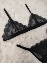 Conjunto de lencería de encaje negro, compuesto por un soutiene triangular de tirantes finos y una bombacha colaless ajustable con tiras laterales.