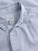 Camisa de manga larga Calvin Klein, confeccionada en sarga de algodón. Presenta cuello abotonado, cierre frontal con botones y logo de la marca bordado sutilmente en el pecho.