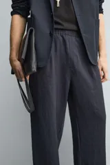 Pantalón negro de corte relajado con cintura elástica ajustable y pliegues en la parte delantera. Presenta bolsillos laterales y bolsillos traseros de parche.