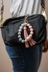 Llavero con pulsera de cuentas redondas de silicona en tonos celeste y gris, con un cubo de madera natural y borla decorativa en color celeste.