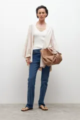 Capa tejida de punto en color natural, con diseño abierto, mangas amplias y terminaciones con volados sutiles.