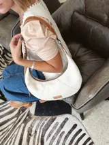 Cartera tipo hobo de cuero color crudo con correa de cuero marrón.