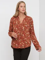 Blusa de manga larga color marrón terracota con estampado floral en tonos rojos, blancos y verdes. Presenta un escote en V con cuello mao y mangas que se pueden ajustar con presilla y botón.