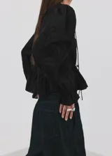 Blusa de algodón negra con detalles florales bordados, cuello en pico con cierre de lazo, manga larga abullonada y diseño recto con vuelo en la cintura.