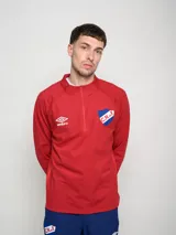 Buzo deportivo de polytraining color rojo, con medio cierre frontal y cuello alto. Presenta el logo de Umbro en el pecho izquierdo y el escudo del Club Nacional de Football en el pecho derecho.