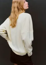 Jersey de punto fino color blanco, con cuello alto, diseño recto y manga larga con detalle fruncido en los hombros.