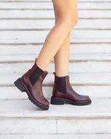 Botas tipo Chelsea de cuero color marrón, con paneles laterales elásticos en negro y tirador trasero en color rojo. Presentan una suela track robusta de goma negra con costuras decorativas en rojo.