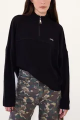Sweater negro de punto con cuello alto y cierre frontal parcial de cremallera, de manga larga y diseño holgado con hombros caída.
