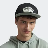 Gorro tipo cap con visera plana, cuerpo negro y visera en color verde grisáceo. Presenta un parche frontal con el logo de la marca Kristobelga Surfboards Company.