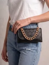 Riñonera negra de diseño acolchado con textura trenzada, cuenta con una cadena decorativa gruesa en color dorado y cierre de solapa.