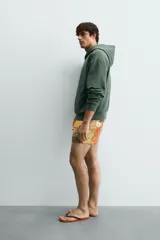 Sudadera con capucha de corte relajado, color verde oscuro, con interior perchado y bordado pequeño de una silla en el centro del pecho.