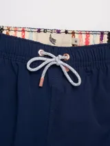 Short de baño azul marino con cintura elástica y cordón blanco con detalles en cobre. Presenta un parche bordado con una flor blanca y roja en la pierna izquierda y un parche con logo en la pierna derecha.