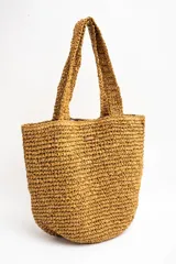 Bolso tipo tote color camel, confeccionado en material trenzado con textura rústica, doble asa de hombro y pequeño aplique metálico con el logo de la marca.