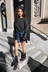 Botín de caña media confeccionado en serraje color marrón oscuro. Presenta un diseño minimalista con pespuntes decorativos, punta redonda y tacón bajo en bloque de madera.