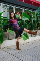 Vestido corto con estampado geométrico en tonos violeta, rojo y negro, confeccionado en jersey elastizado con efecto gamuzado. Presenta cuello redondo y mangas 3/4 con puños abotonados. La falda es de corte irregular con volados.